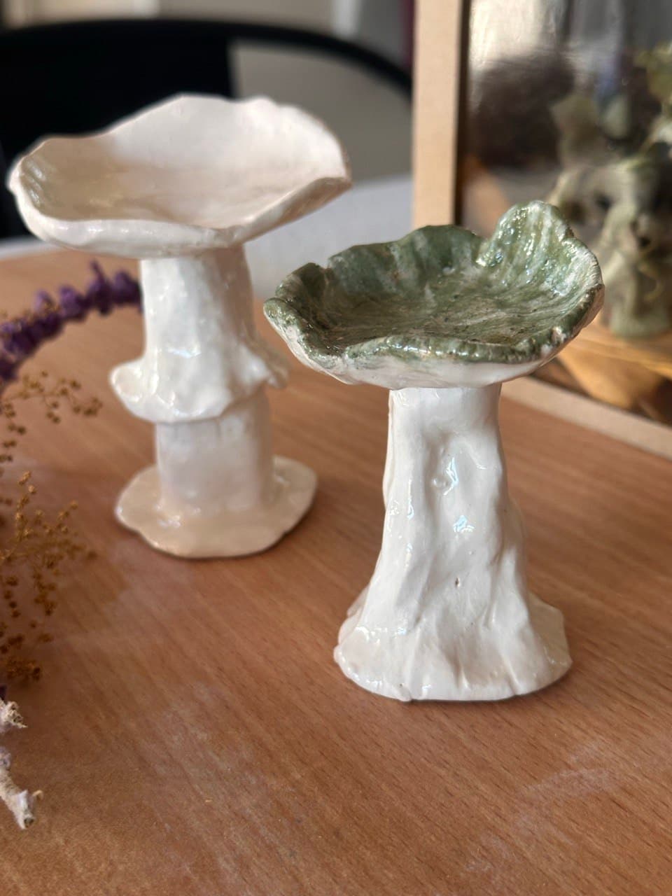 Los mismos dos hongos vistos de cerca: adelante, el de sombrero verde salvia con el borde ondulado y el tallo blanco con vetas en relieve; atrás, el blanco con su pollerita en el tallo