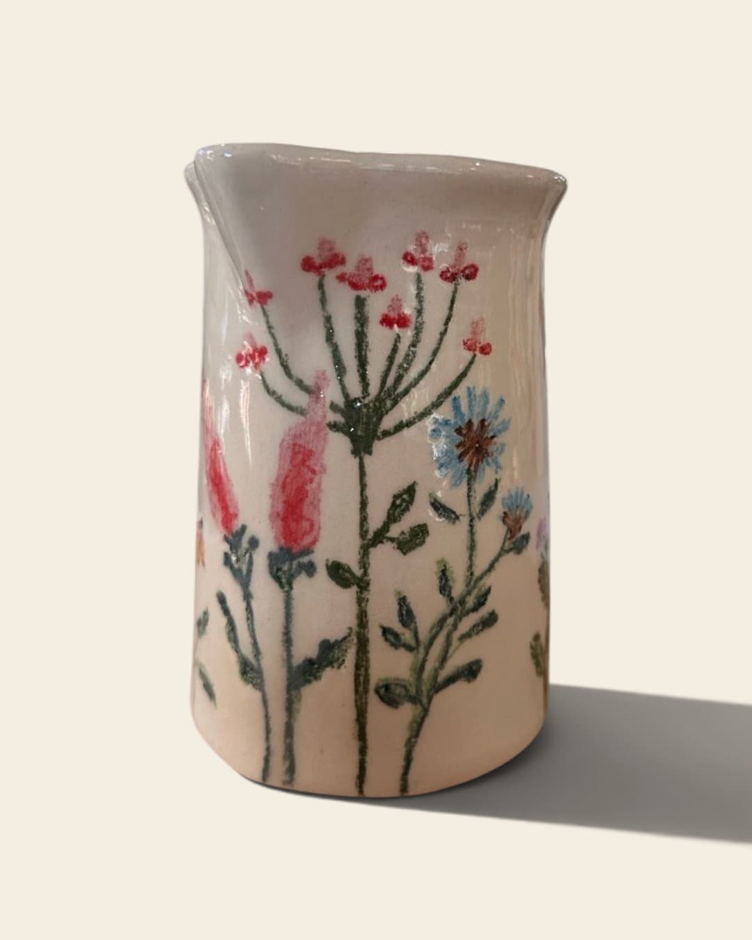 Jarra de cerámica color crema pintada a mano con flores silvestres de tallos finos en rojo, rosa y celeste
